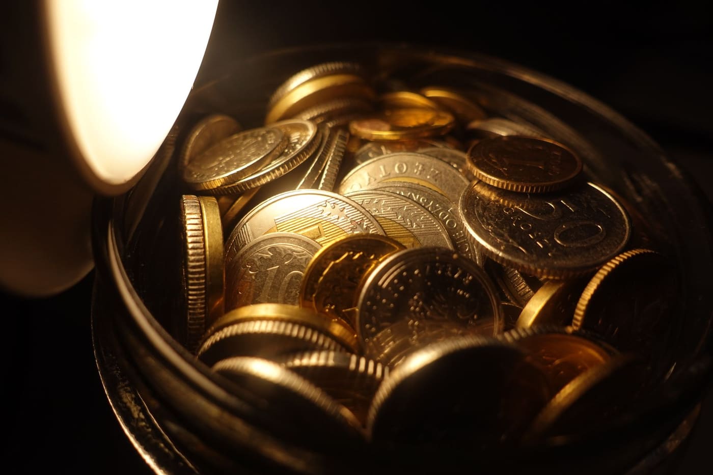 Close view of assorted coins filling a glass jar in warm light