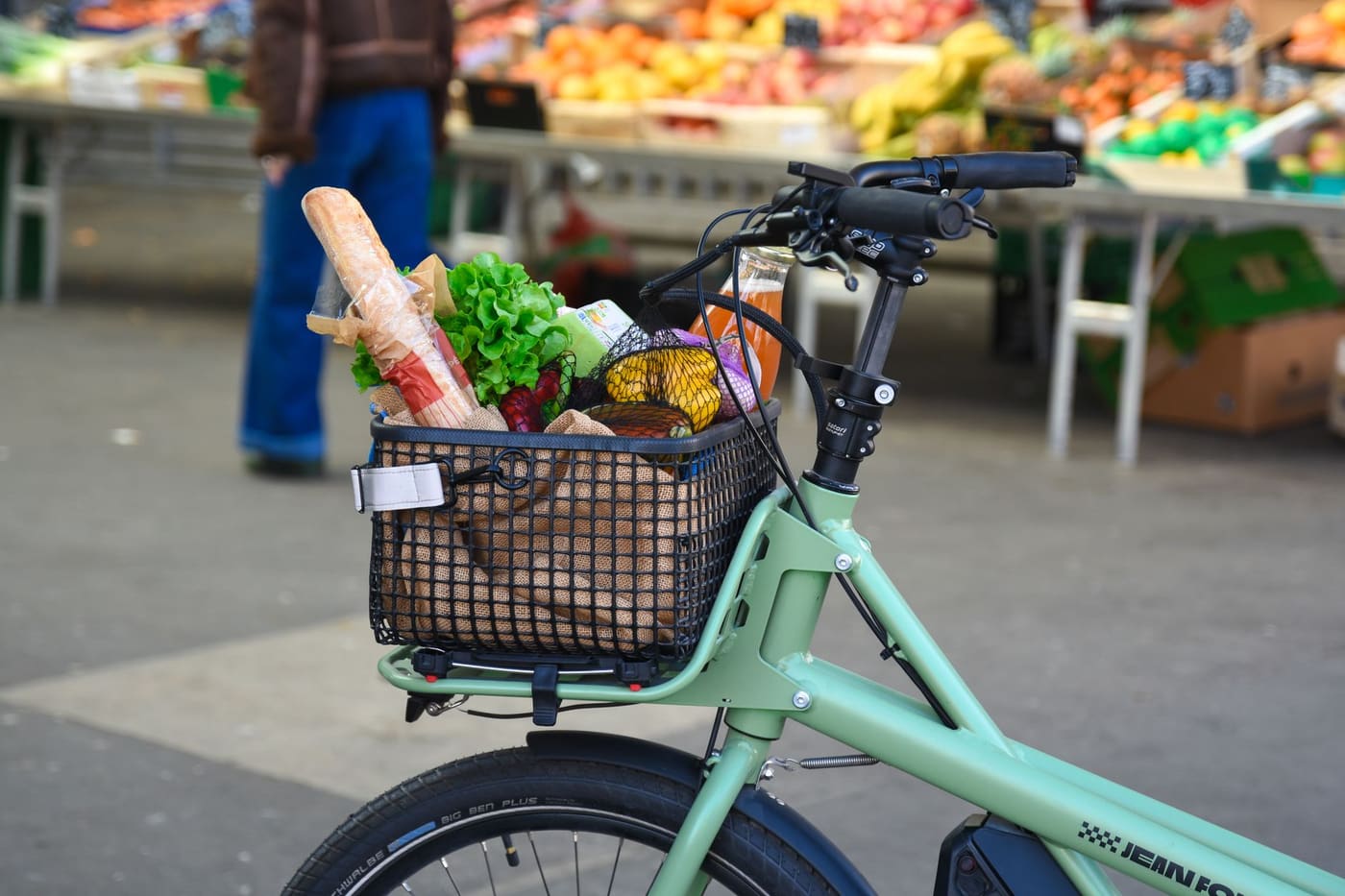A pale green bicycle with a basket of groceries parked at an outdoor market