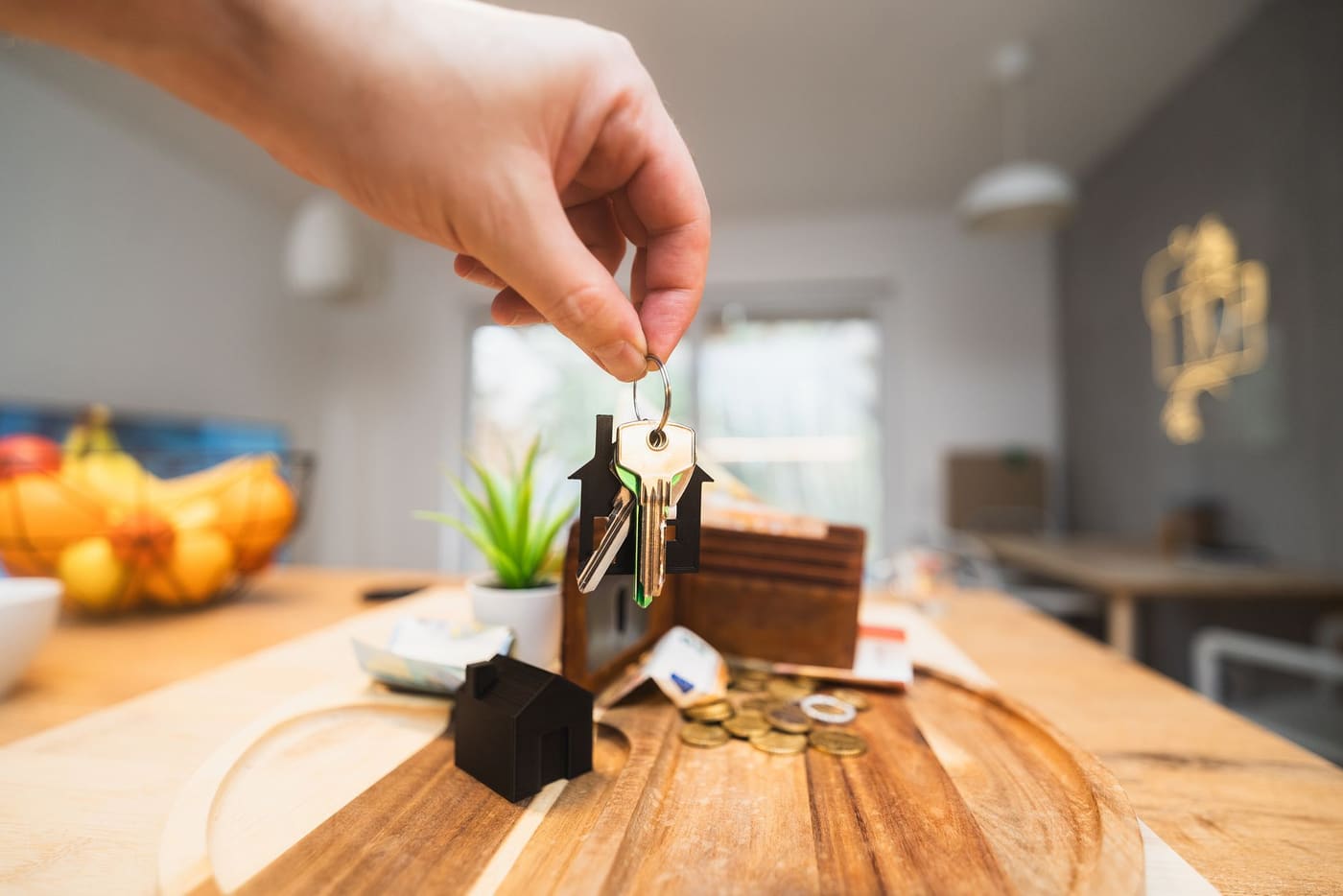 A hand holding a set of house keys above a wooden table in a bright living room