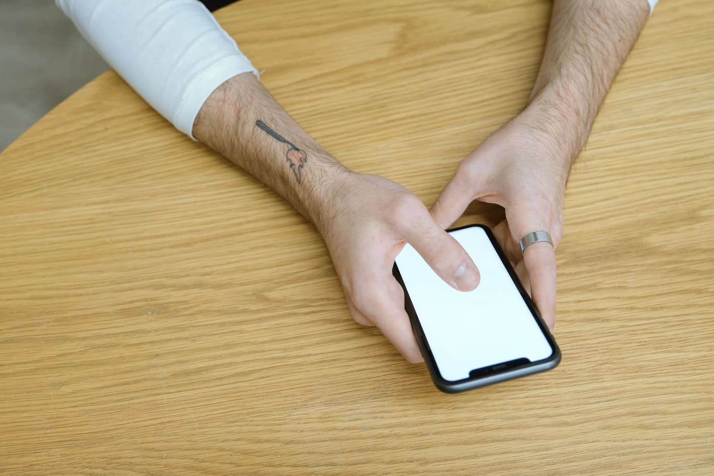 Two hands holding a smartphone with a blank screen over a wooden table