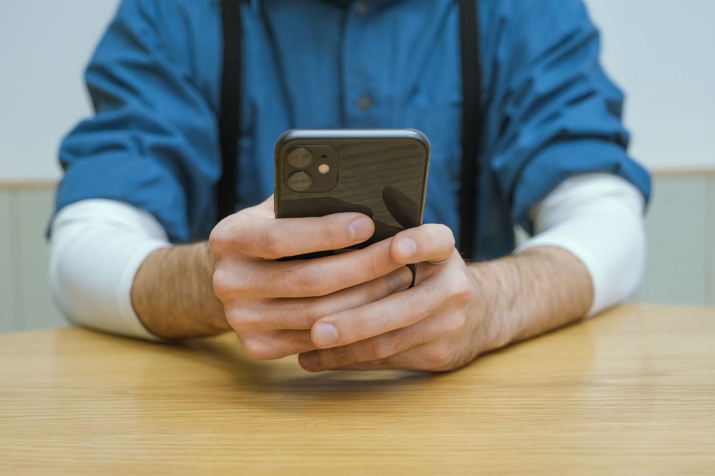 A man in a blue shirt holding a smartphone over a table