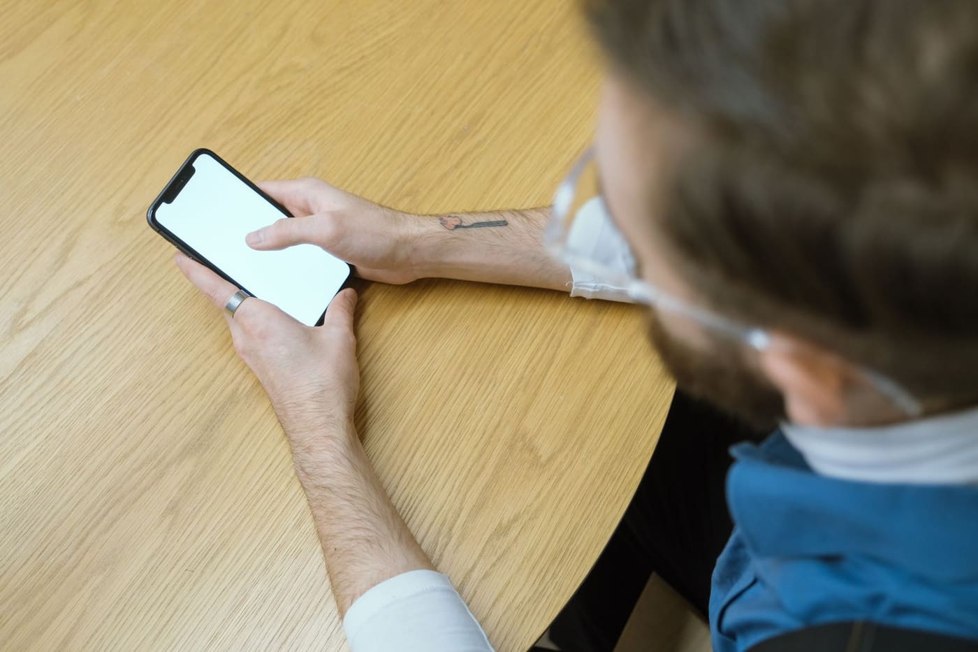 A person holding a smartphone with a blank screen at a wooden table, seen from above