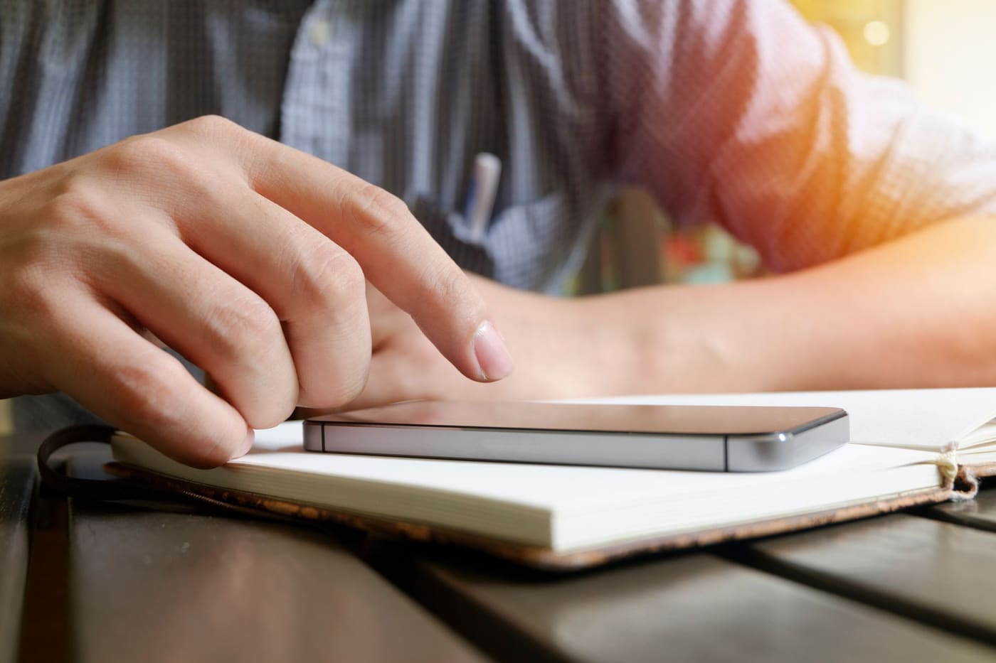 A hand resting on a smartphone lying on an open notebook on a desk