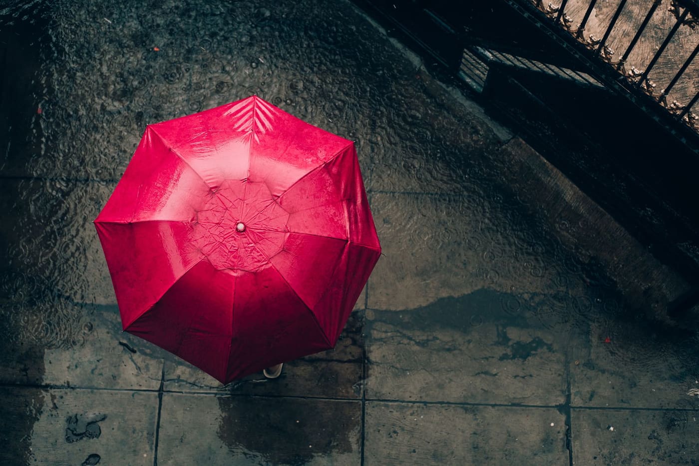 Aerial view of a person holding a red umbrella on a rainy city street