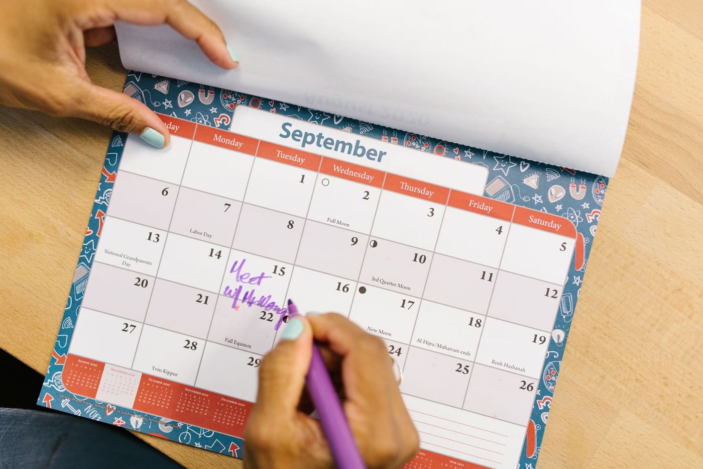 A hand writing a note on a September desk calendar with a purple pen